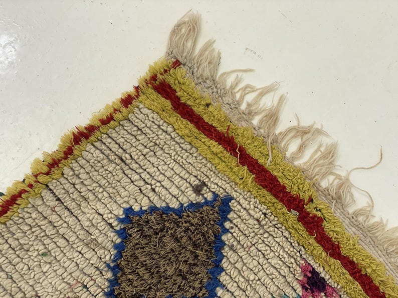 a close-up view of a colorful, textured rug with a fringed edge and a geometric pattern.