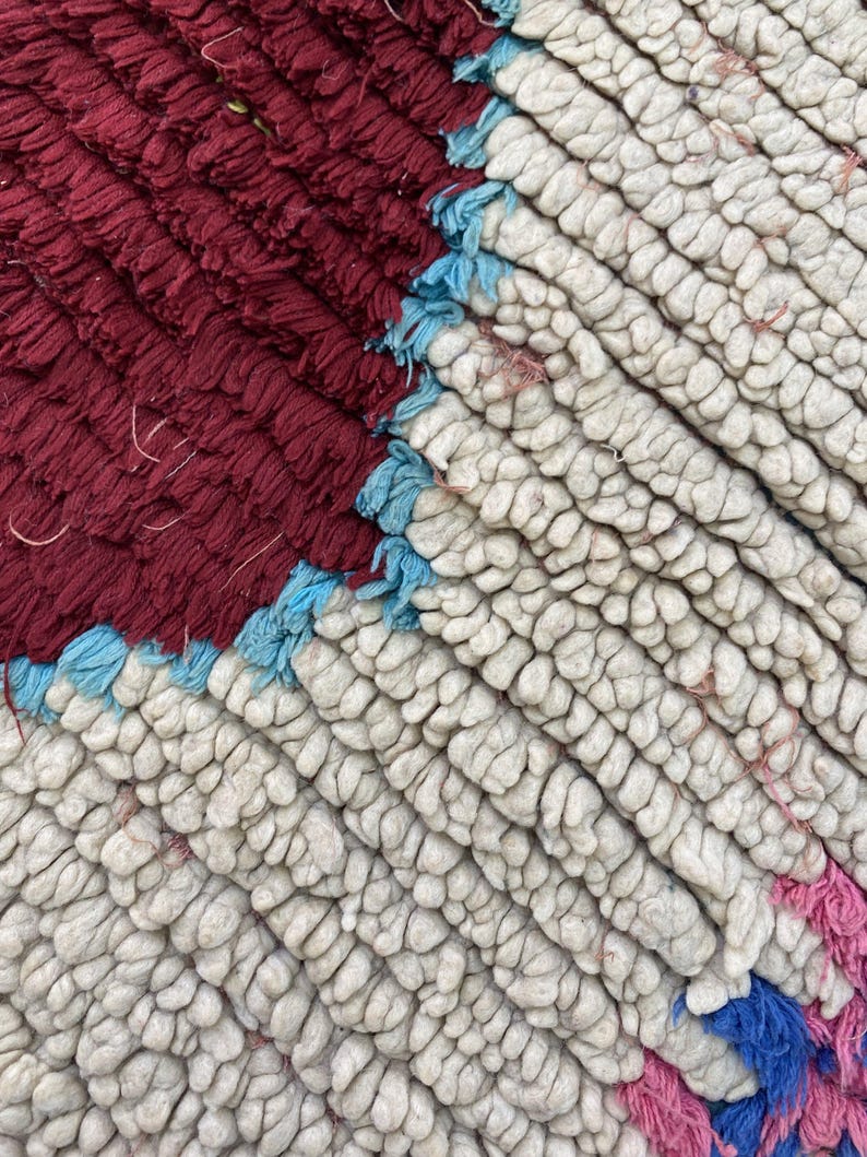 a close-up view of a textured fabric with a red and blue color scheme. The fabric appears to be a woven or knitted material, with a mix of white, red, and blue colors. The image does not contain any discernible text or countable objects, and the focus is on the intricate patterns and textures of the fabric.