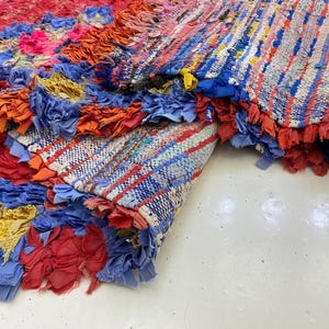 a vibrant, multicolored rug with a variety of patterns and textures, including red, blue, yellow, and orange. The rug appears to be a handmade piece, with a mix of different materials and colors creating a visually striking and intricate design.