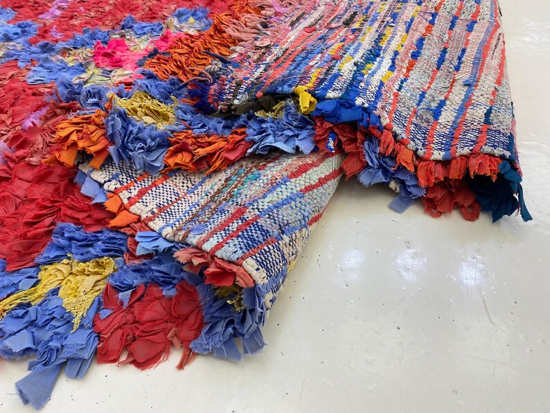 a vibrant, multicolored rug with a variety of patterns and textures, including red, blue, yellow, and orange. The rug appears to be a handmade piece, with a mix of different materials and colors creating a visually striking and intricate design.