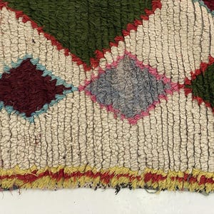 a close-up view of a colorful, textured rug with a diamond pattern. The rug has a mix of green, red, and yellow colors, creating a vibrant and eye-catching design.