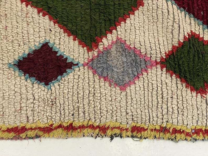 a close-up view of a colorful, textured rug with a diamond pattern. The rug has a mix of green, red, and yellow colors, creating a vibrant and eye-catching design.
