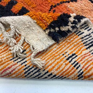 a close-up view of a vibrant, multicolored rug with a striking pattern of orange, black, and white stripes.
