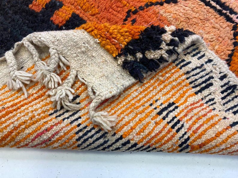 a close-up view of a vibrant, multicolored rug with a striking pattern of orange, black, and white stripes.