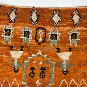 a vibrant, intricately designed rug with a striking pattern of geometric shapes and figures in shades of orange, black, and white.