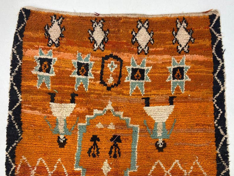 a vibrant, intricately designed rug with a striking pattern of geometric shapes and figures in shades of orange, black, and white.