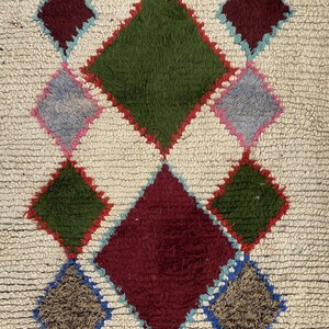 a vibrant, colorful rug with a diamond pattern. The rug is composed of various geometric shapes and colors, including shades of green, red, and yellow. The rug appears to be a traditional, handmade textile, with a textured surface that adds depth and dimension to the design.