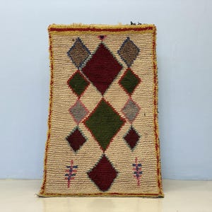 A colorful, geometric rug with a diamond pattern and various shades of green, red, and beige.