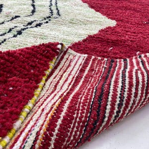 a close-up view of a vibrant, multicolored rug with a striking red and white pattern. The rug has a textured surface with a mix of red, white, and black colors, creating a visually appealing and eye-catching design.