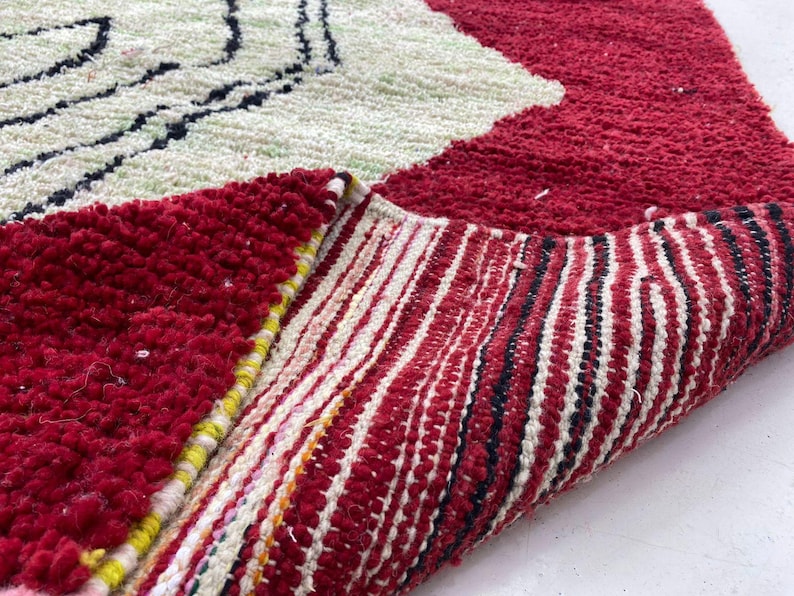 a close-up view of a vibrant, multicolored rug with a striking red and white pattern. The rug has a textured surface with a mix of red, white, and black colors, creating a visually appealing and eye-catching design.