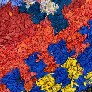The image is a vibrant and colorful collage composed of various fabrics and materials in shades of red, blue, yellow, and orange. The arrangement of the different colors and textures creates a visually striking and dynamic composition.