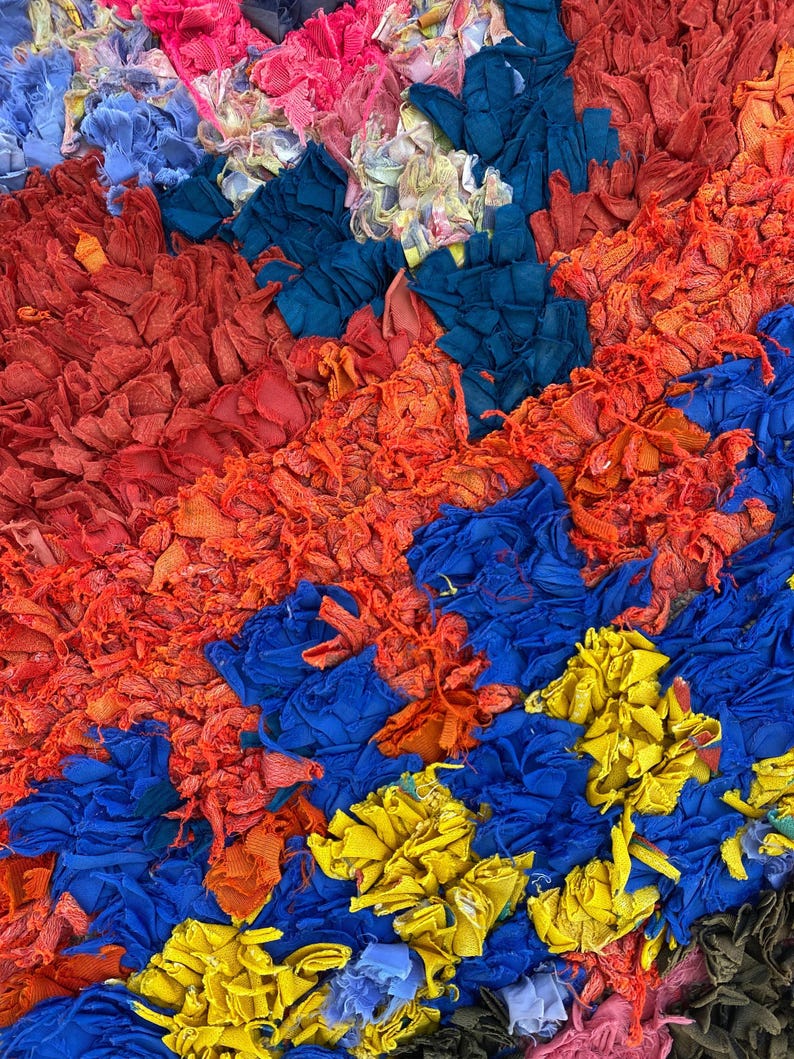 The image is a vibrant and colorful collage composed of various fabrics and materials in shades of red, blue, yellow, and orange. The arrangement of the different colors and textures creates a visually striking and dynamic composition.
