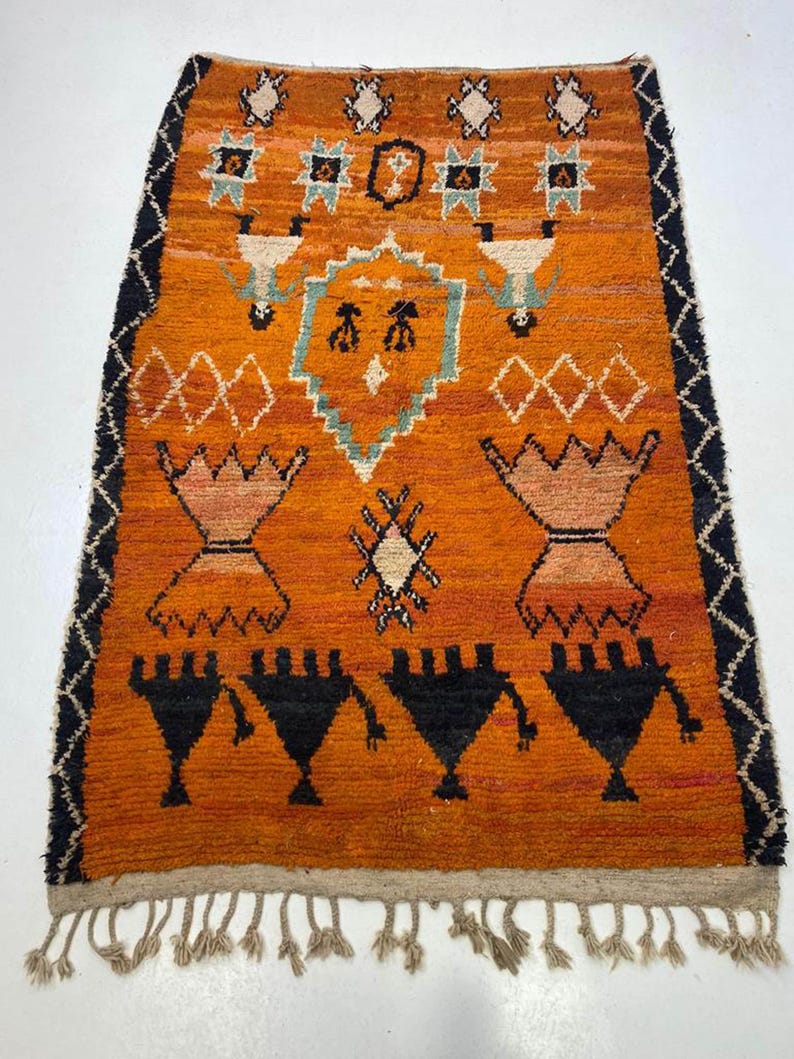 a vibrant, intricately designed rug with a striking orange and black color scheme. The rug is adorned with various geometric patterns and shapes, creating a visually captivating piece of art.