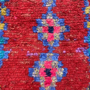 a vibrant, colorful rug with a striking pattern of red, blue, and yellow hues. The rug is adorned with a variety of shapes and textures, creating a visually captivating and intricate design.