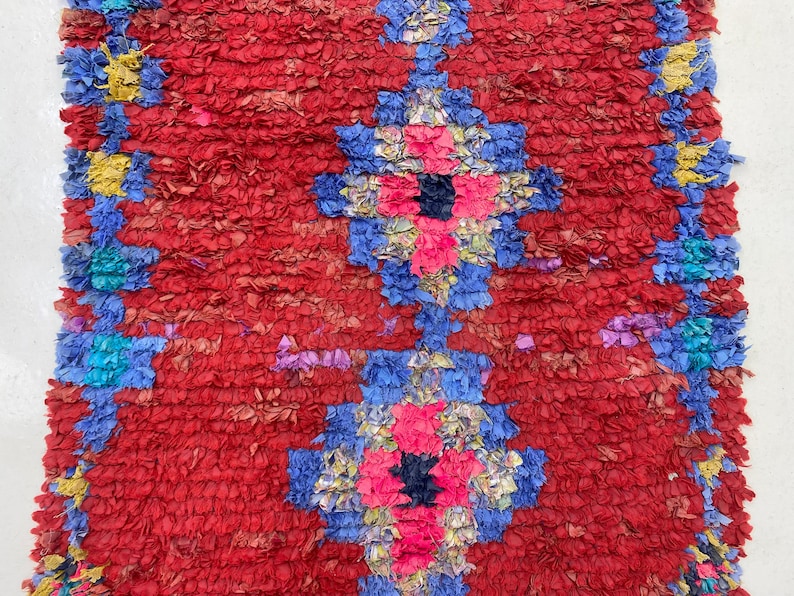 a vibrant, colorful rug with a striking pattern of red, blue, and yellow hues. The rug is adorned with a variety of shapes and textures, creating a visually captivating and intricate design.