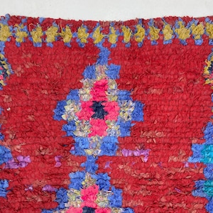 a vibrant, colorful rug with a red and blue geometric pattern. The rug has a textured, plush appearance and is adorned with a variety of colors, including red, blue, yellow, and pink.