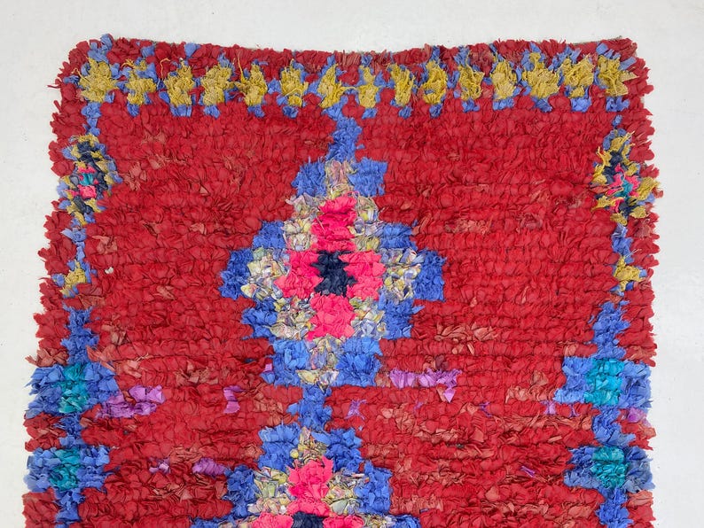 a vibrant, colorful rug with a red and blue geometric pattern. The rug has a textured, plush appearance and is adorned with a variety of colors, including red, blue, yellow, and pink.