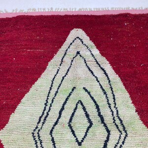 May include: A red and white geometric rug with a diamond pattern. The rug has a red background with a large white diamond shape in the center, outlined in black. The diamond has a green center.