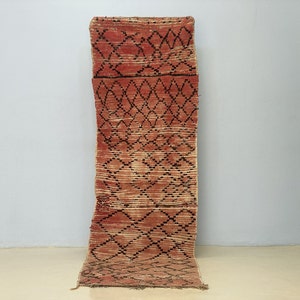 Peut inclure: Un tapis rectangulaire tissé à la main avec un motif géométrique en losanges. Le tapis présente une palette de couleurs rouge, noir et beige. Le motif est symétrique, avec le motif en losanges qui se répète sur toute la longueur du tapis. Le tapis est probablement fait de fibres naturelles.