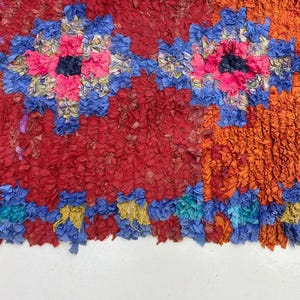 The image is a vibrant and colorful textile with a repeating pattern of red, blue, and orange hues. The pattern is composed of various shapes and textures, creating a visually striking and intricate design.