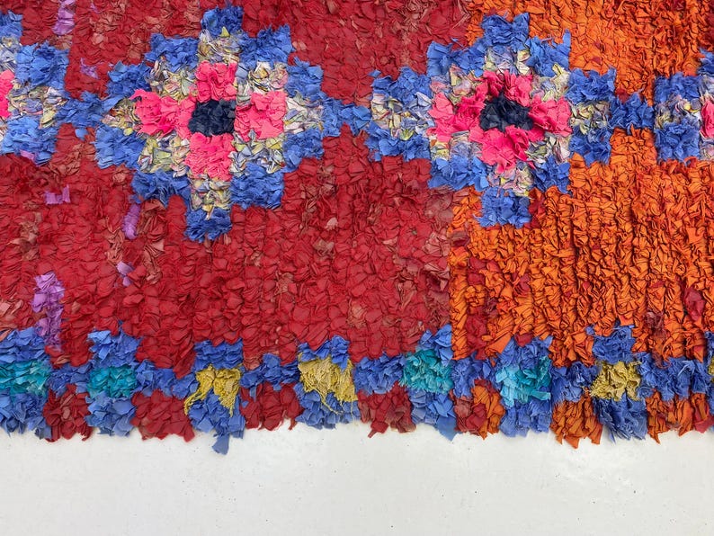 The image is a vibrant and colorful textile with a repeating pattern of red, blue, and orange hues. The pattern is composed of various shapes and textures, creating a visually striking and intricate design.