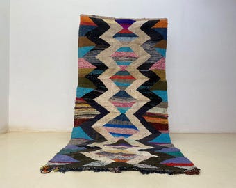 May include: A vibrant, geometric rug featuring a zig-zag design in blue, pink, black, and cream. The rug has a textured finish and a fringed edge. This decorative rug is suitable for home decor.