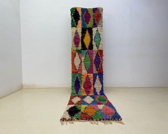 May include: A colorful, rectangular rug with a diamond pattern. The rug features a variety of colors, including green, yellow, pink, and blue. The rug is made of a shaggy material and has a fringe on the bottom. The rug is approximately 60 inches long.