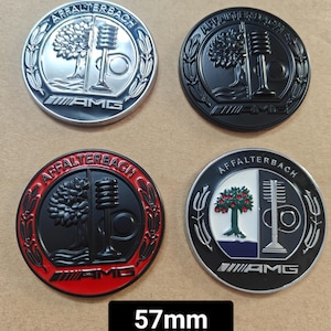 Könnte beinhalten: Vier 57 mm runde Metallembleme mit dem Text "Affalterbach AMG" und einem stilisierten Baum- und Rennstreckendesign. Zwei Embleme sind silber mit schwarzen Designs, und zwei Embleme sind schwarz mit silbernen Designs. Eines der schwarzen Embleme hat einen roten Außenring.