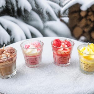 Könnte beinhalten: Vier Glaskerzen in kleinen Bechern, die jeweils mit wachsartigen Dekorationen verziert sind, die an Lebensmittel erinnern. Die Kerzen haben braune, rosa, rote und gelbe Farben mit strukturierten Wachswirbeln und fruchtartigen Formen.