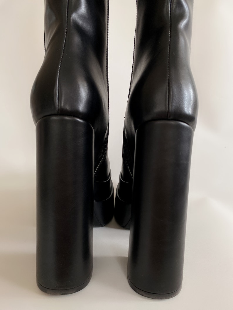 May include: A pair of black leather heeled boots with a chunky block heel. The boots have a zip on the back and a pointed toe.