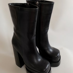May include: A pair of black leather platform boots with a chunky heel. The boots have a square toe and a zip on the inside of the ankle.