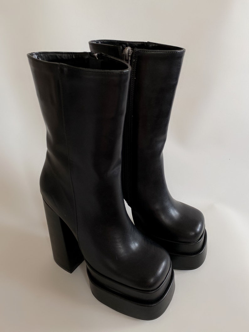 May include: A pair of black leather platform boots with a chunky heel. The boots have a square toe and a zip on the inside of the ankle.