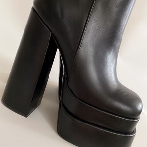 May include: Black leather platform boots with a thick, square heel. The boots have a chunky platform sole and a pointed toe.