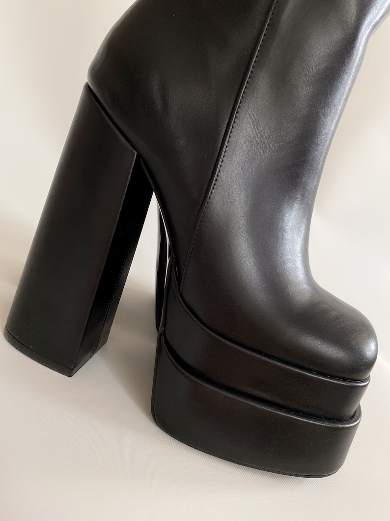 May include: Black leather platform boots with a thick, square heel. The boots have a chunky platform sole and a pointed toe.