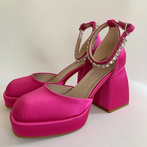May include: Pink satin platform heels with a chunky block heel and a rhinestone ankle strap.