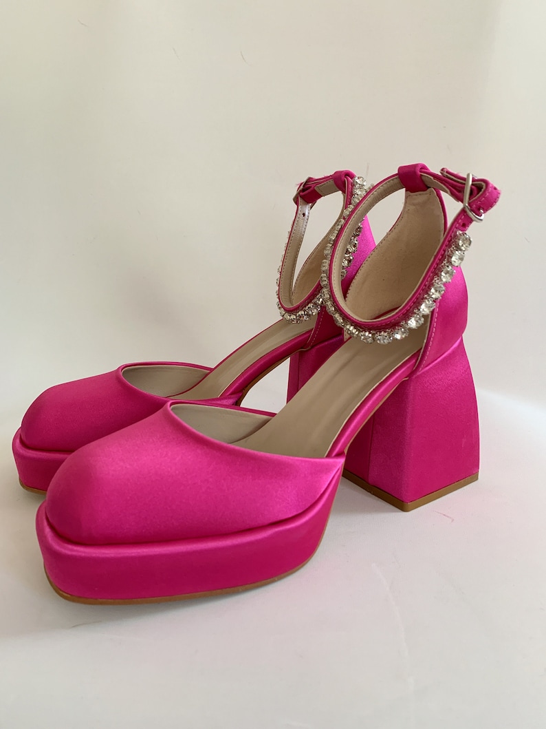 May include: Pink satin platform heels with a chunky block heel and a rhinestone ankle strap.