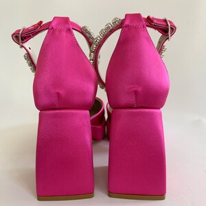 May include: A pair of pink satin heeled sandals with a chunky block heel and a crystal embellishment on the ankle strap.
