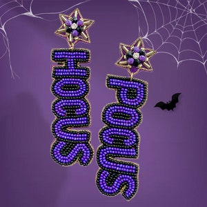 May include: Purple beaded earrings with gold accents and a star charm. The earrings spell out "Hocus" and "Pocus" in a bold, 3D font.