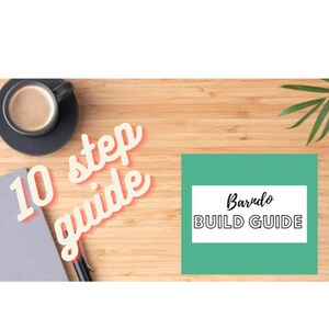 Puede incluir: Una mesa de madera con una taza de café, un cuaderno, un bolígrafo y una tarjeta verde con el texto "Barndo BUILD GUIDE" y el texto "10 step guide" en rosa y naranja.