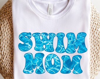 Könnte beinhalten: Weißes T-Shirt mit dem Text "Swim Mom" in blauen Buchstaben mit einem Wasserwellenmuster.