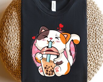 May include: Black t-shirt with a cartoon illustration of a cat drinking boba tea. The cat is white with orange and black markings. The boba tea is in a clear cup with brown tapioca pearls.
