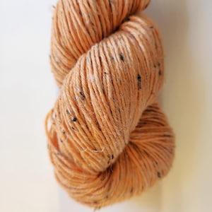 以下が含まれることがあります： 黒い斑点のあるオレンジ色の糸の玉。糸は柔らかくふわふわしていて、編み物や編み物に最適です。