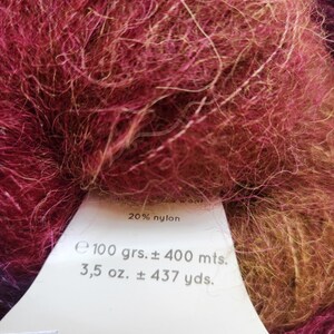 Pu&ograve; includere: Primo piano di un gomitolo di filato nei toni del bordeaux, rosa e oro. Il filato ha un aspetto soffice e strutturato. Un'etichetta indica che il filato &egrave; 20% nylon, 100 grammi e circa 400 metri. Ideale per progetti di maglia e uncinetto.
