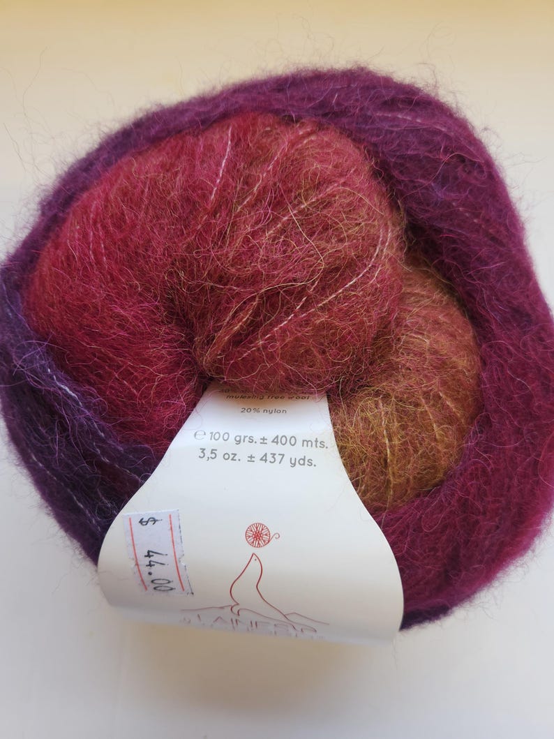 Pu&ograve; includere: Un gomitolo di filato multicolore nei toni del viola, rosso e oro. L'etichetta indica che il filato pesa 100 grammi e misura circa 400 metri. Il filato &egrave; un mix di materiali, tra cui il 20% di nylon.