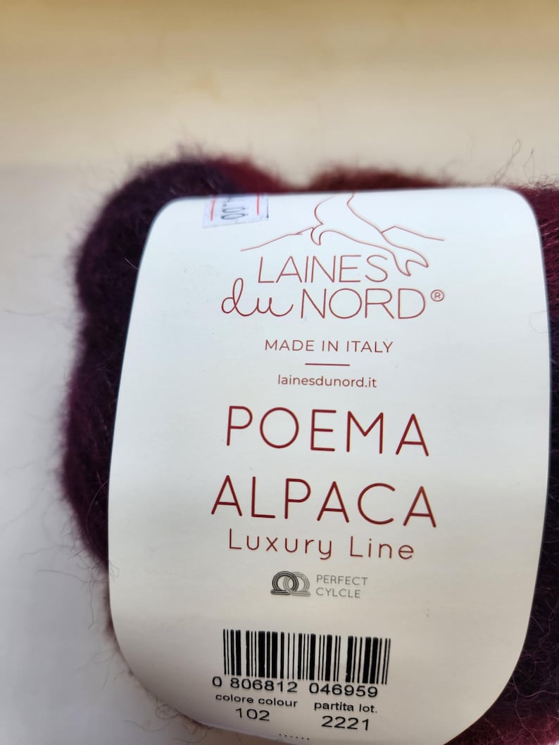 Pu&ograve; includere: Primo piano di un gomitolo di filato bordeaux scuro con un'etichetta. L'etichetta recita "LAINES du NORD" e "POEMA ALPACA Luxury Line". Il filato &egrave; prodotto in Italia e ha un codice a barre.