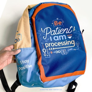 May include: Blue and orange backpack with the text "Be Patient I am processing" and "Stay Positive" on the front. The backpack has a light blue and tan colored strap.