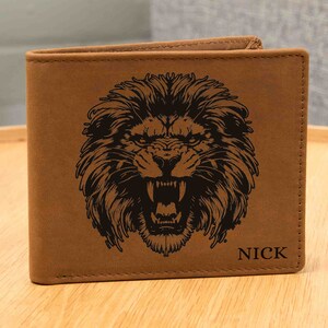 May include: A brown leather wallet featuring a detailed black illustration of a roaring lion's head. The name "NICK" is printed in black on the lower right corner. The wallet is closed and appears to be made of a textured material.