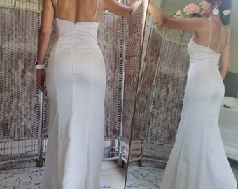 Puede incluir: Un vestido blanco de satén con la espalda descubierta y tirantes finos. El vestido es ajustado y tiene una falda larga y fluida.