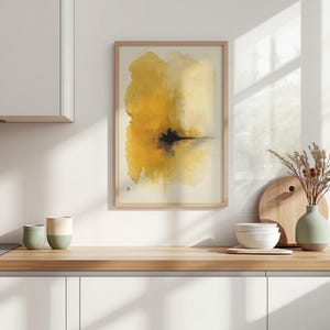 May include: Abstract art print in a wooden frame. The artwork features a blend of yellow and black watercolor-style paint. The painting is displayed on a white wall above a wooden countertop, with kitchen accessories in the foreground.