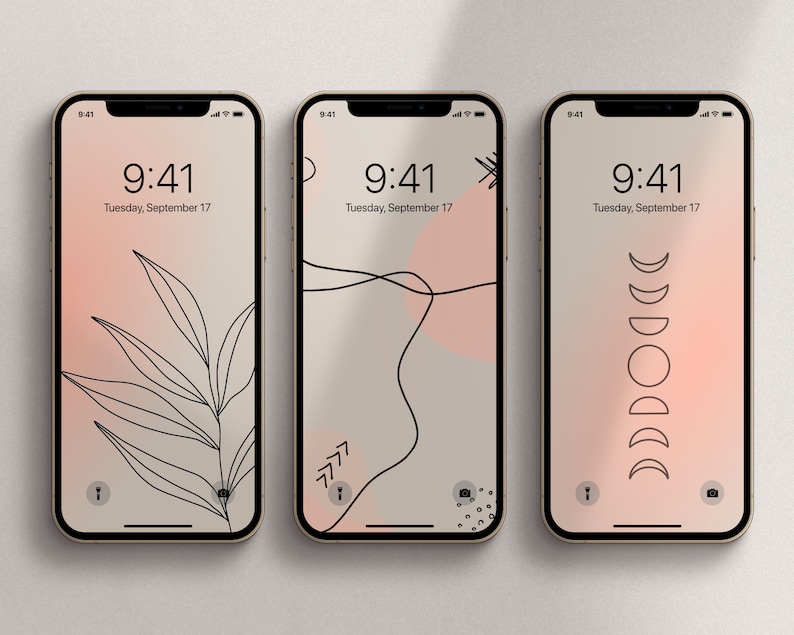May include: Three iPhone mockups with different minimalist phone wallpapers. The first wallpaper features a black line drawing of a leaf on a gradient background of pink and beige. The second wallpaper features a black line drawing of a curved line and a pink circle on a beige background. The third wallpaper features a black line drawing of a crescent moon in various phases on a gradient background of pink and beige. All three mockups display the time as 9:41 and the date as Tuesday, September 17.